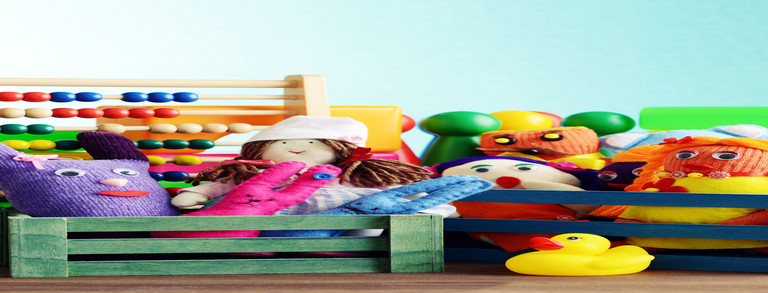 Eine Nahaufnahme verschiedener Spielzeuge in kleinen bunten Holzkisten. Man sieht Stoffpuppen, eine Gummiente, Spielfiguren und einen Abakus mit bunten Holzperlen.