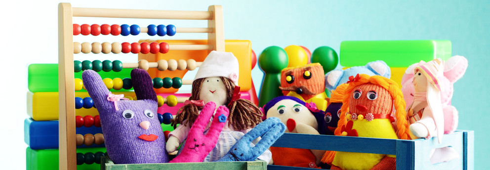 Sprachtherapeutisches Ambulatorium Eine Nahaufnahme verschiedener Spielzeuge in kleinen bunten Holzkisten. Man sieht Stoffpuppen, eine Gummiente, Spielfiguren und einen Abakus mit bunten Holzperlen.